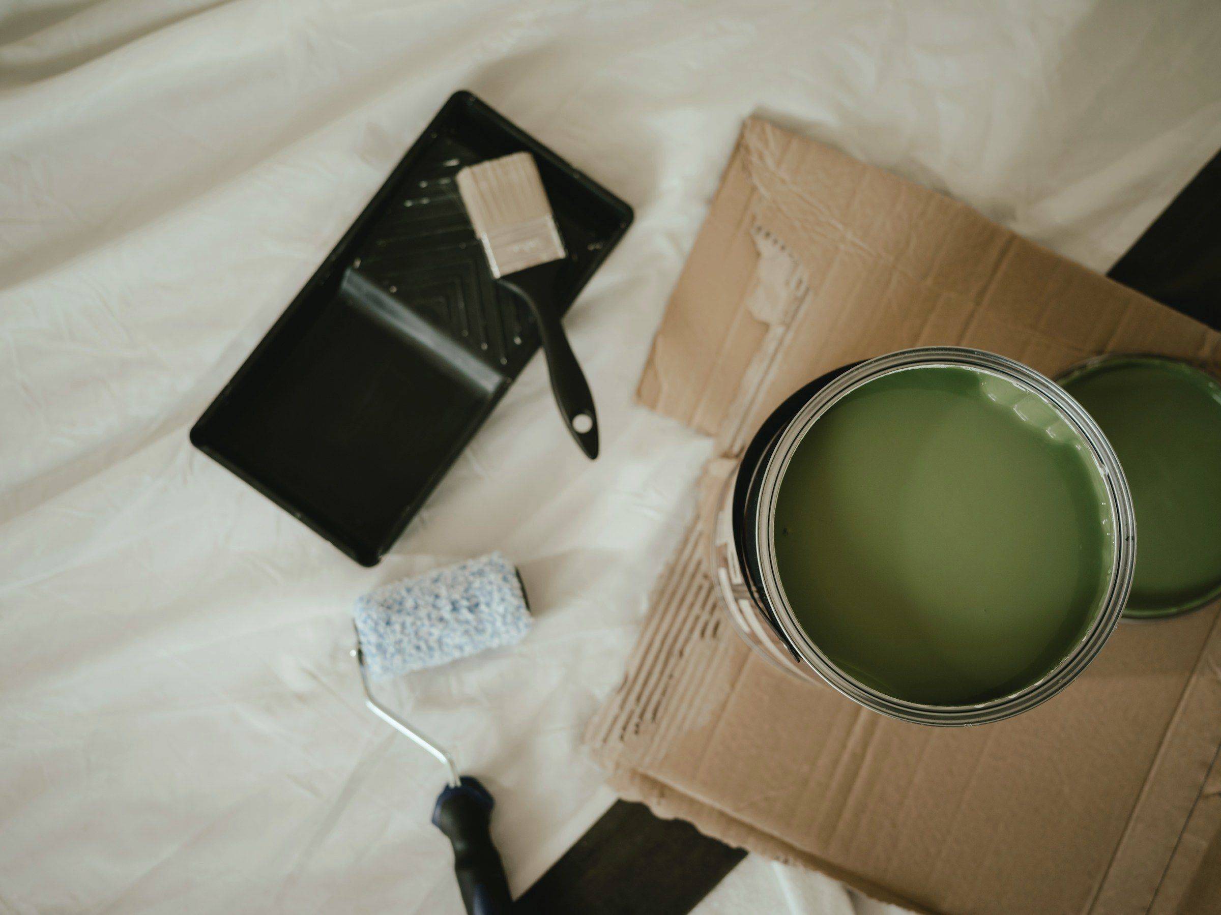 Tin of sage green paint with a brush and roller tray